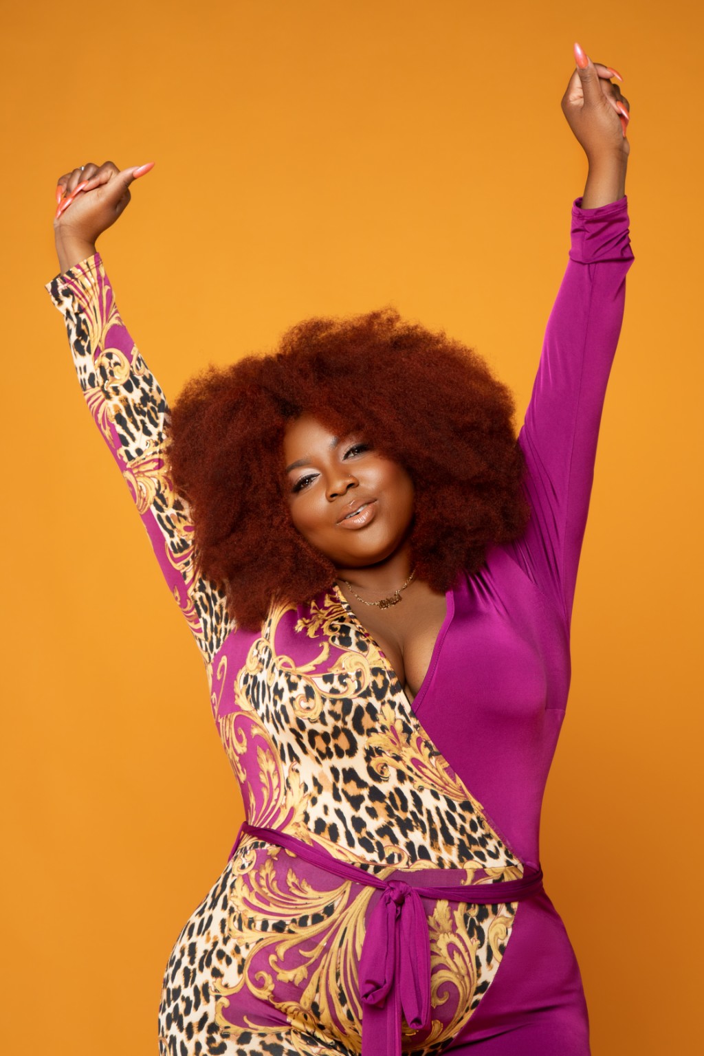 Lisia.S. wearing purple and gold with her arms raised against an orange background